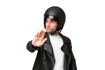 Young caucasian man with a motorcycle helmet isolated on green chroma background making stop gesture and disappointed