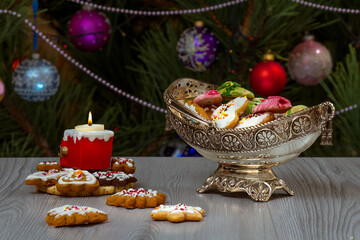 Metal vase with gingerbread cookies and fir tree with toy balls on the background.
