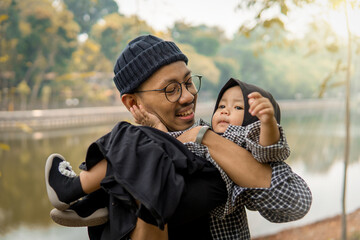 Asian father and son playing together with a moment of full happiness in the background of the lush trees.