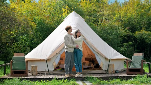 A couple hugging each other and talking on a tent terrace at glamping. Lush forest around