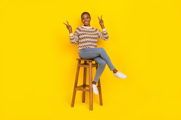 Fototapeta premium Full size portrait of friendly positive lady sit chair hands fingers show v-sign isolated on yellow color background