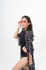 Studio portrait photo of a young beautiful elegant Brazilian female model lady wearing black color swimsuit bikini, sunglasses and beach scarf posing with a series moments of emotion and gesture 