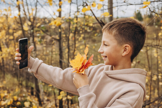 Teenager boy with autumn bouquet of maple leaves taking selfie photos with his smartphone.