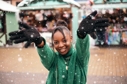 African American Woman Standing Street Outside Near Christmas Tree Fair Market, Playing Catches With Hands Up, White Snow Falling Down. New Year Atmosphere, Winter Vacation, Cold Weather
