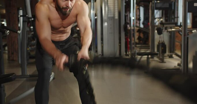 An athlete trains in a gym with battle ropes