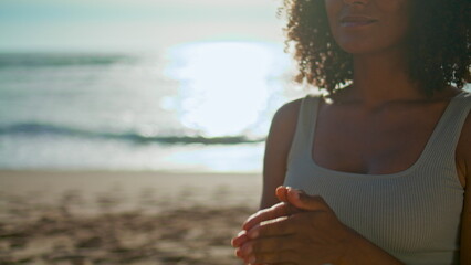 Woman performing namaste position at sunrise beach close up. Girl meditating.