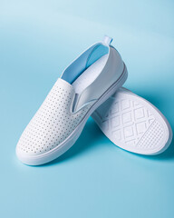 Promotional photo of pair of white women's moccasins on light blue background.