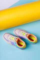 Pair of fashionable bright sports shoes for teens standing on orange-blue background.