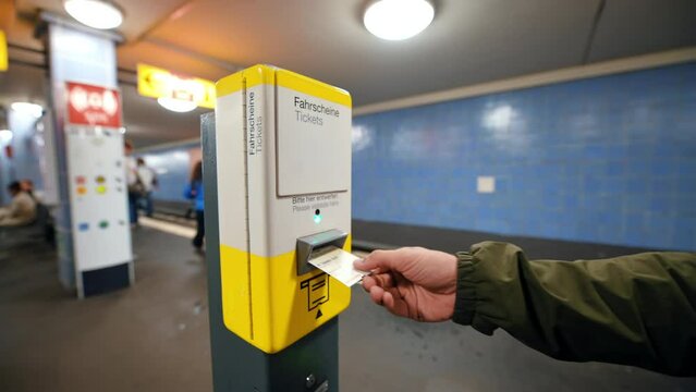 A man inserts a ticket into a machine in the Berlin underground, Germany. People walking at the station