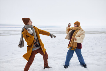 Full length portrait of couple playing snowball fight outdoors in winter, copy space