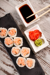 Sushi roll covered with chopped salmon and caviar is served on rectangular black slate.