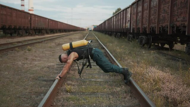 Young muscular man with balloon dragger on his back does exercise plank on rails and quickly pulls his knees in turn to his chest