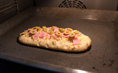 Pizza baking with ham and olives