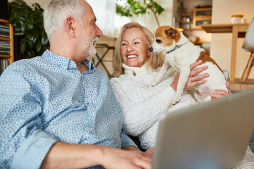Couple of seniors with dog and laptop pc on sofa