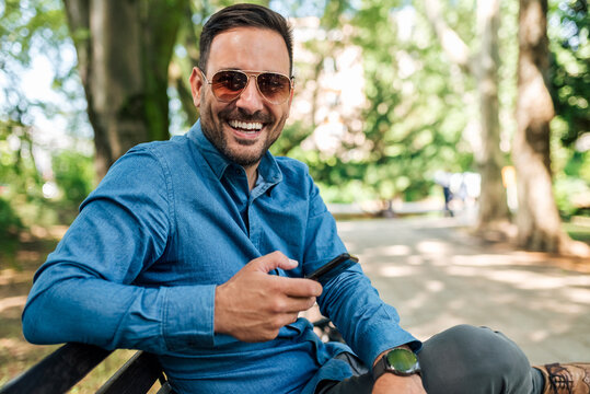 Portrait of stylish young adult man, holding his phone, smiling for the picture.