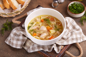Chicken soup with noodles, potatoes and carrots. Delicious homemade clear broth soup, served with dill and white bread.