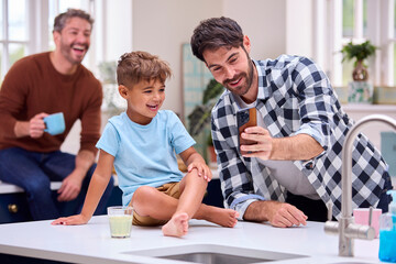 Same Sex Family With Two Dads Taking Selfie In Kitchen With Son Sitting On Counter