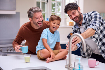 Same Sex Family With Two Dads Taking Selfie In Kitchen With Son Sitting On Counter