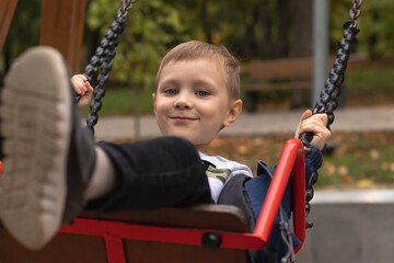 Little adorable kid boy riding a swing in a park. Happy childhood concept
