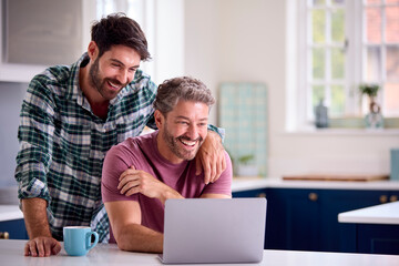 Same Sex Male Couple Using Laptop At Home To Check Finances Book Holiday Or Shop
