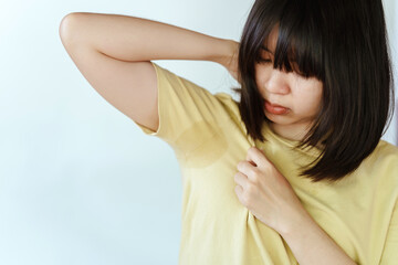 A woman wearing a yellow shirt is sweating in her armpits.