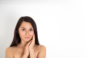 Fototapeta na wymiar A natural portrait of a well-groomed young brunette woman with nude makeup. Gentle Beauty keeps her hands close to her face. White background place for text