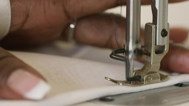 Close shot of woman feeding fabric through a sewing machine as the needle stitches
