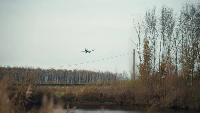A large passenger plane comes in to land over an autumn lake and fields outside the city. There is a runway nearby. A warm and windy autumn day near the airport.