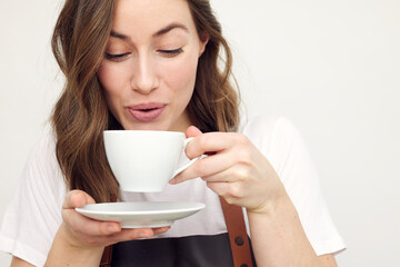 Close-up portrait of beautiful young barista woman drinking and tasting some hot coffee. Isolated on white background looking professional and serving coffee. Concept: Want a break?