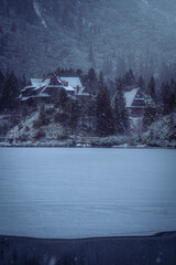 Small hut in the distance on the other side of a frozen lake lake in winter snowing