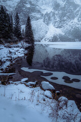 Moody winter photo of a frozen lake surrounded by high mountains and pine trees