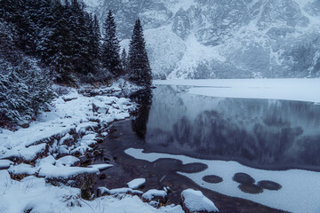 Moody winter photo of a frozen lake surrounded by high mountains and pine trees
