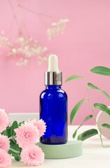 Fototapeta na wymiar Blue cosmetic bottle and flowers. Bottle of cosmetic serum or essential oil. Minimal background layout