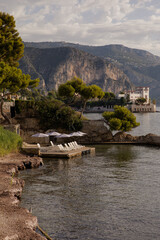 Fototapeta premium View of the sea coast against the background of the mountains. Dawn over the picturesque coast. Sun loungers and umbrellas waiting for holidaymakers. Ideal place to relax