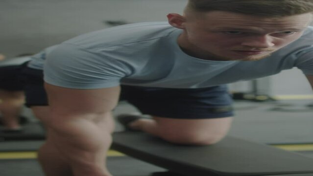 Vertical close up shot of strong man in sportswear doing kettlebell single arm rows on gym bench