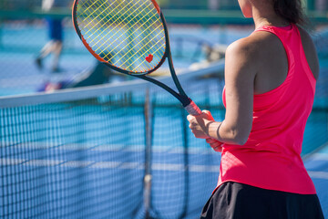 A girl plays tennis on a court with a hard blue surface on a summer sunny day