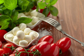 Mozzarella cheese with basil and tomatoes on an old wooden table.