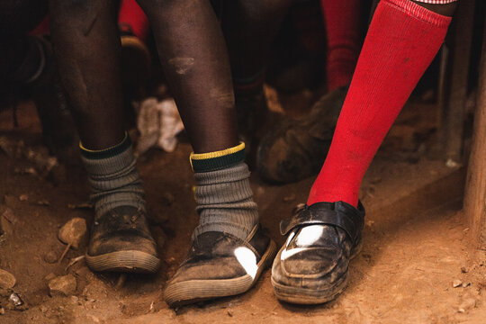 Photograph of the legs and shoes of some African students, in a school in the slum of Nairobi in Kenya. The classrooms are poor and without floors; the boys are wearing worn and old clothes.