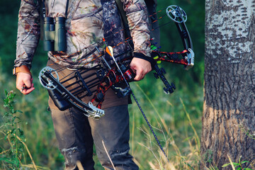 Close up shot of a hunter dressed in camouflage clothing holding a modern bow.