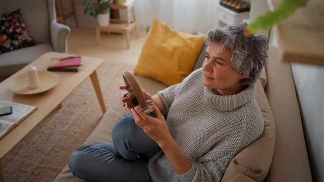 Mature woman at home, listening to music on sofa.