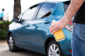 A man in jeans with a bottle of whiskey in his hand tries to get behind the wheel of a car.