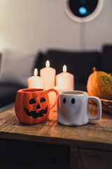 Pareja de tazas de fantasma y calabaza colocadas junto a decoración y golosinas de halloween