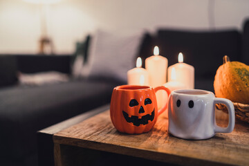 Pareja de tazas de fantasma y calabaza colocadas junto a decoración y golosinas de halloween