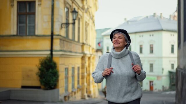Mature woman tourist walking in historical town, smiling.