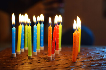 Colorful happy birthday candles burning on brown chocolate cake on dark background.
