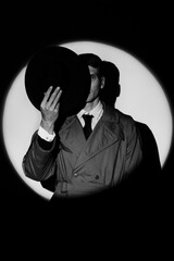 A dark silhouette of a male detective in a coat and hat in the noir style. A dramatic portrait in...