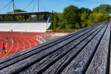 Close view of the structure of a wooden bench. Sports stadium out of focus.