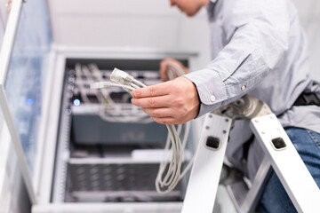 Male technician's hand holds group of white network cables before connecting to port switch.