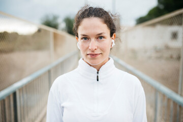 Portrait of young woman in sportswear listening music with wireless headphones on a urban bridge before working out