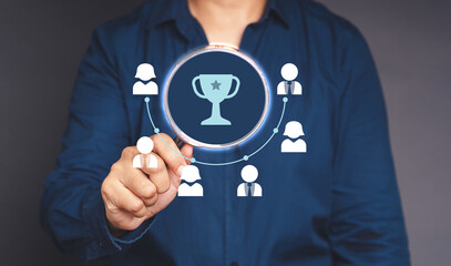 Close-up of hand businessman holding a magnifying glass looking a trophy of the winner award and people icons of teamwork